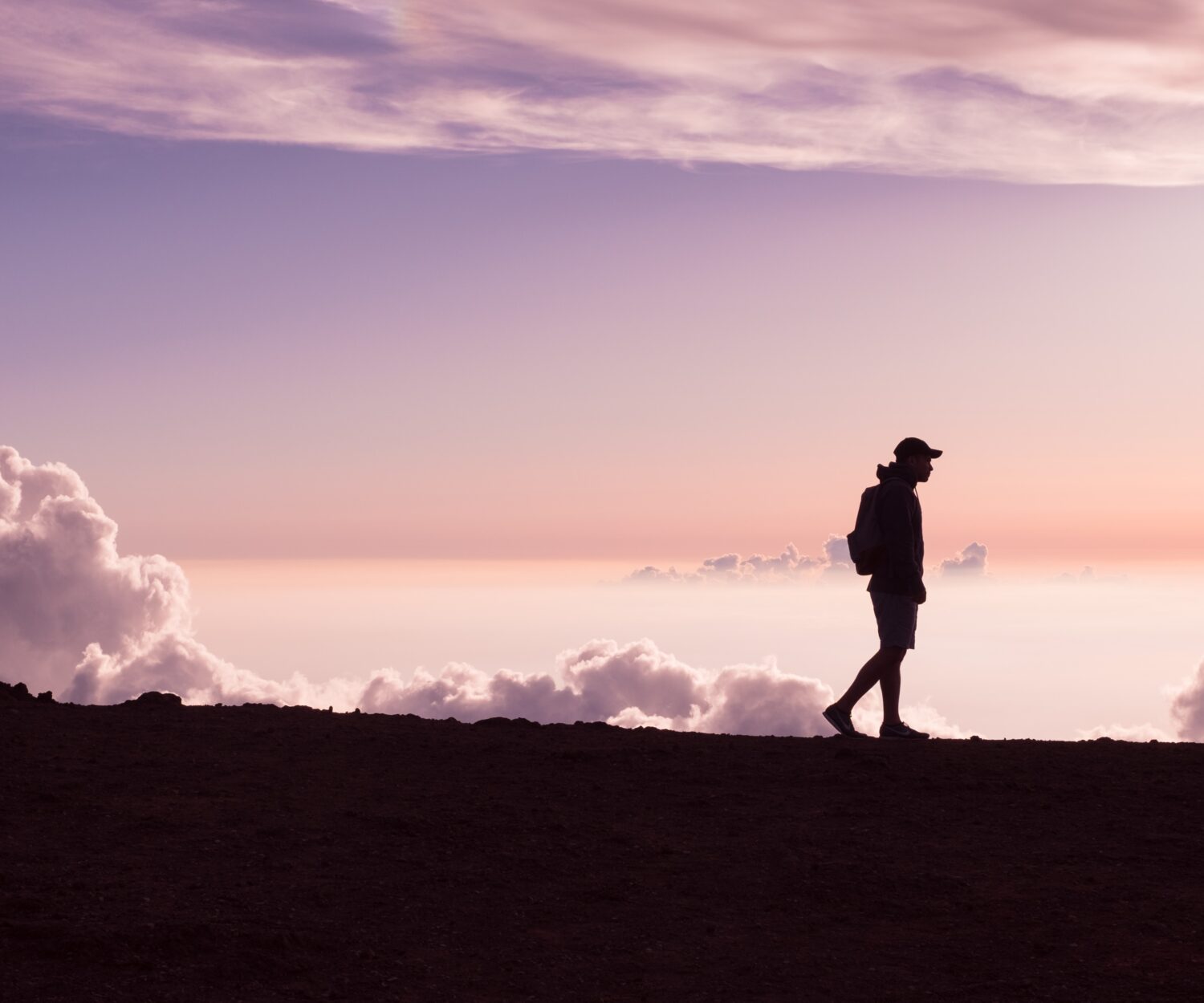 silhouette of person walking under white clouds