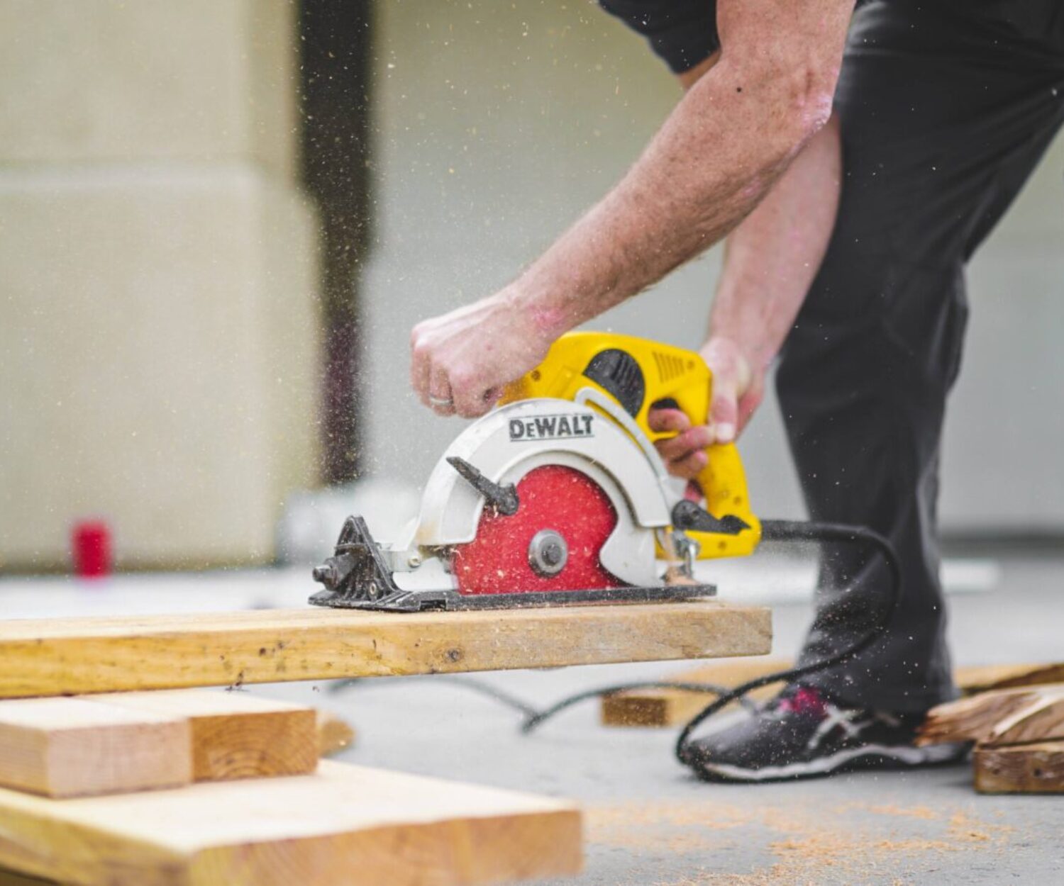 man in black sweatpants using DEWALT circular saw and cutting a wood plank
