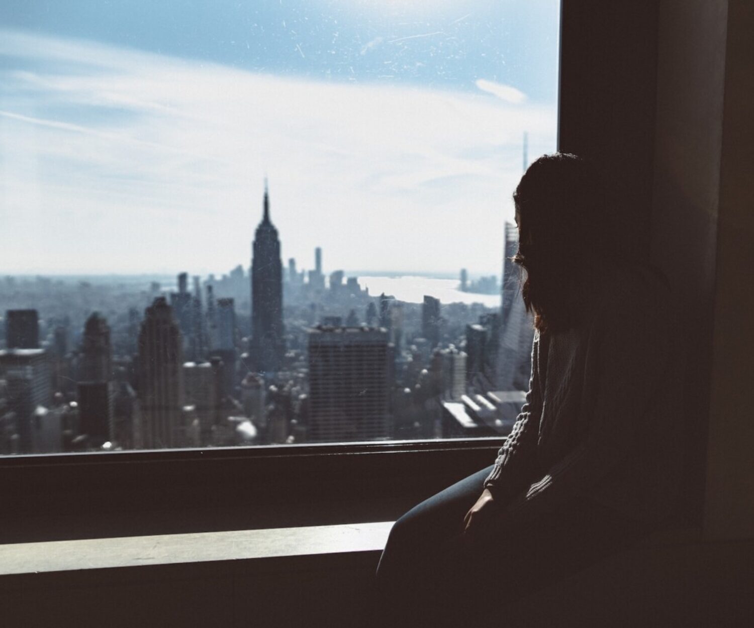 woman sitting on window edge looking at Empire State tower