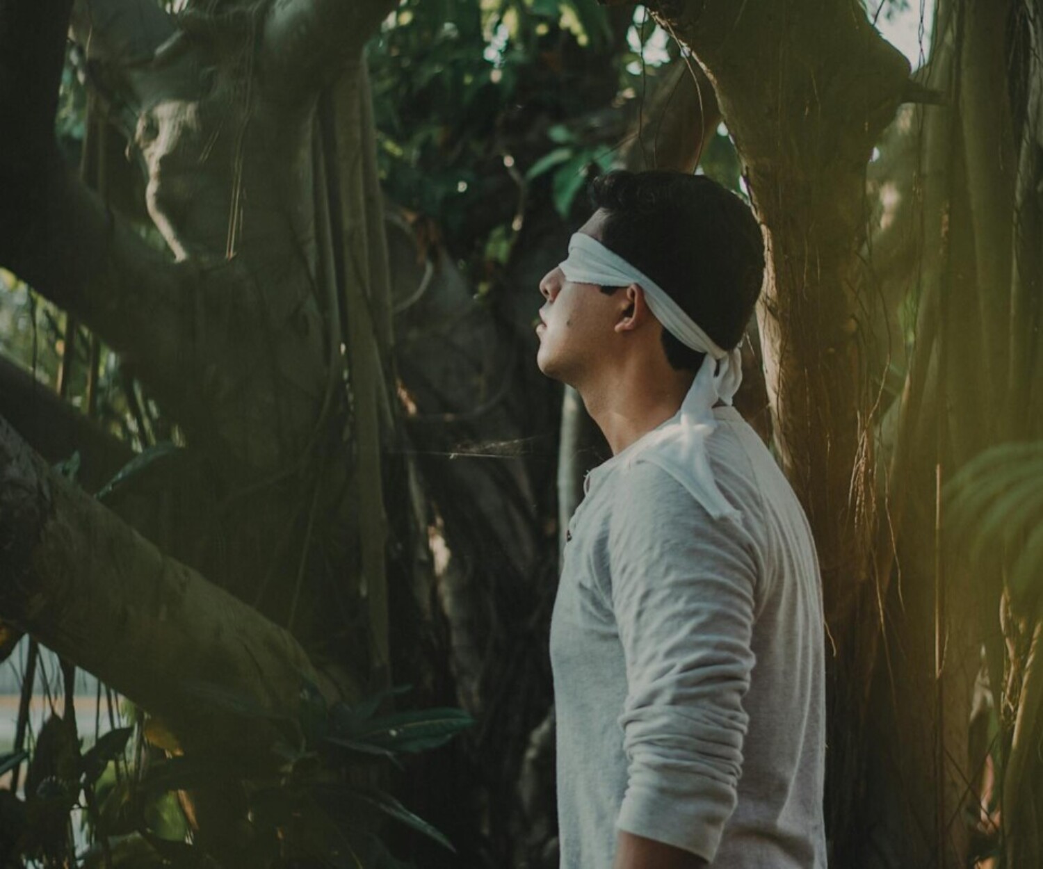 A man stands blindfolded in a serene forest, exploring nature.