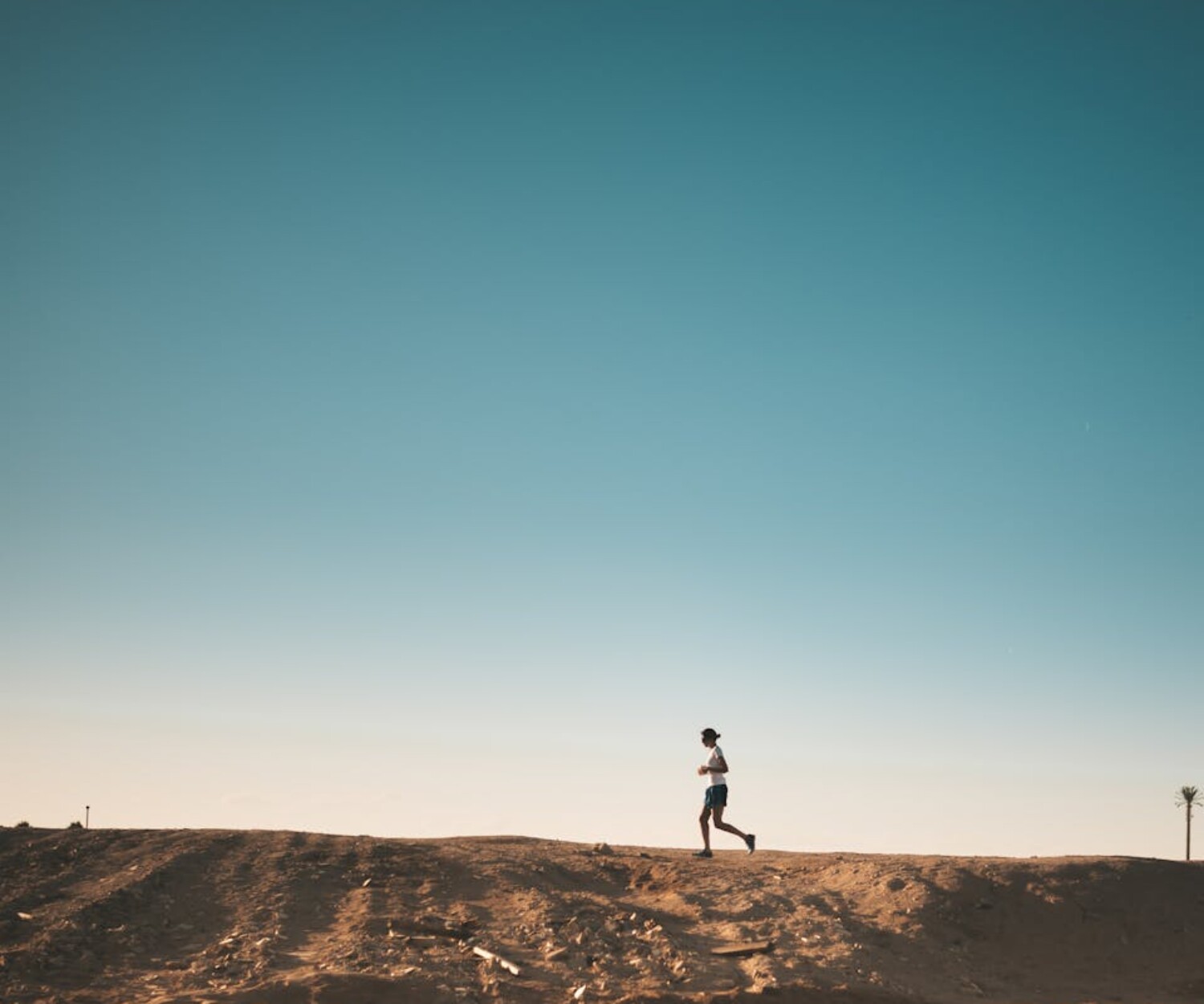 A person jogs on a sandy path with a vast blue sky above, capturing movement and freedom.