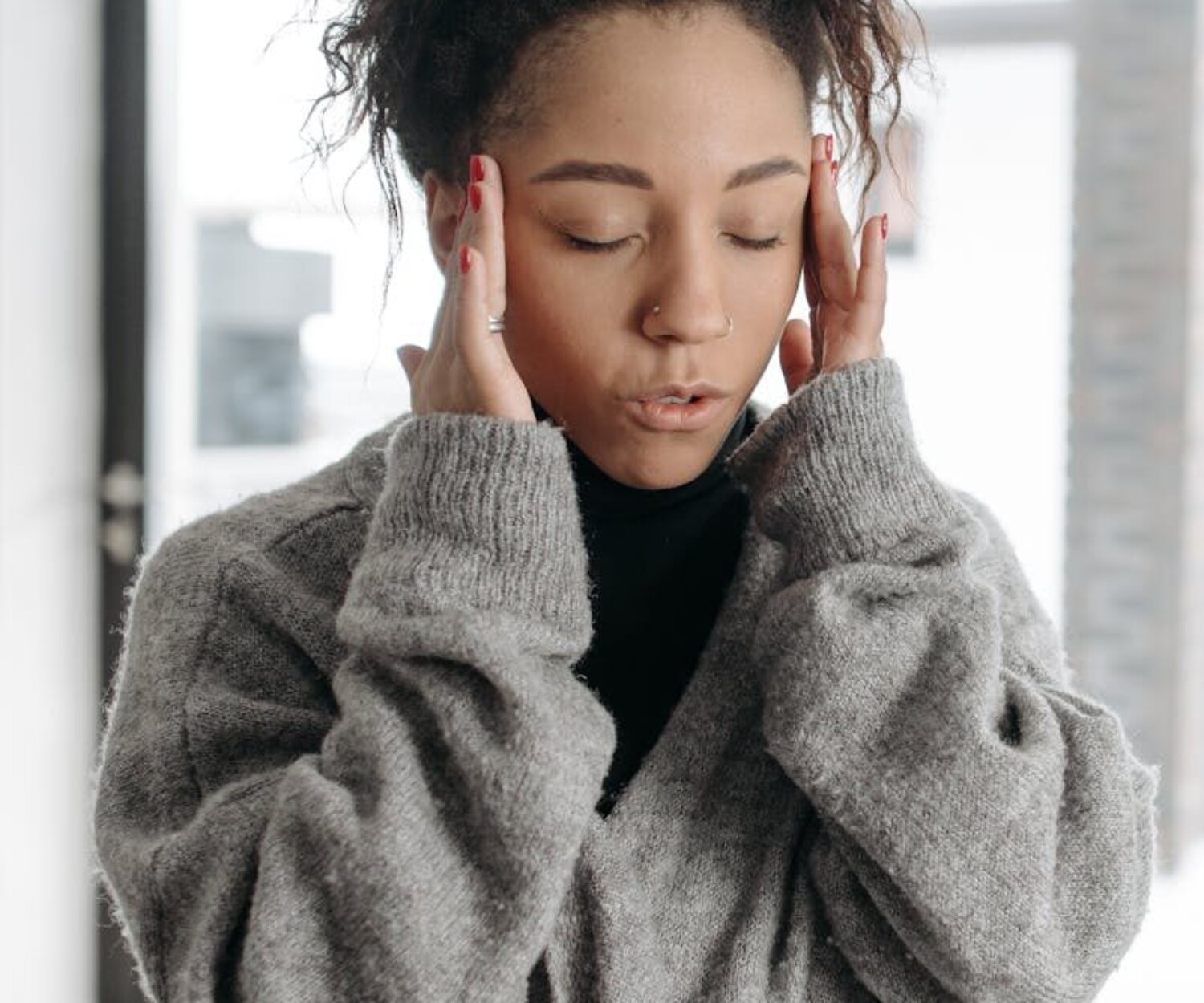 Young woman indoors showing signs of illness, touching her temples in discomfort.