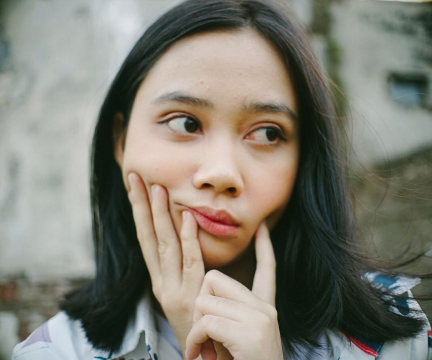 Contemplative young woman with hands on face, outdoors setting, casual wear.